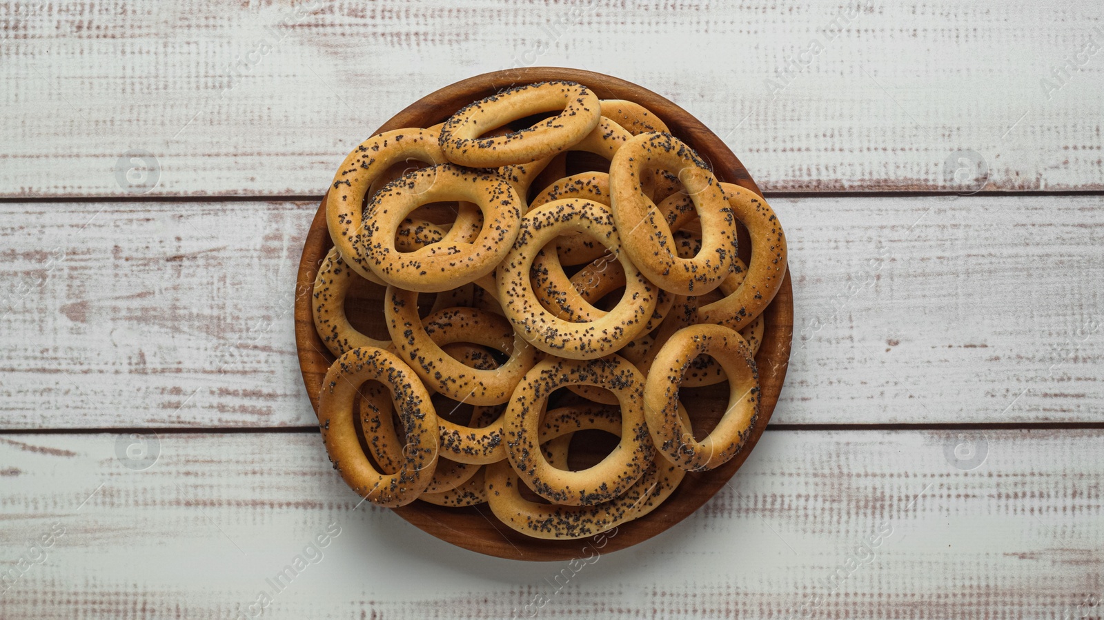 Photo of Plate with delicious ring shaped Sushki (dry bagels) on white wooden table, top view