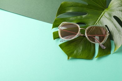Photo of Stylish sunglasses and tropical leaf on color background, space for text