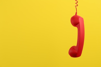 Photo of Red corded telephone handset hanging on yellow background, space for text. Hotline concept