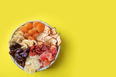 Wicker basket with different dried fruits on yellow background, top view. Space for text