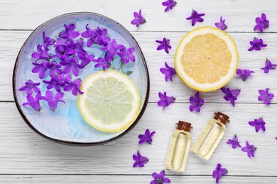 Bowl with water, lemon, purple flowers and bottles of essential oils on white wooden table, flat lay. Spa composition