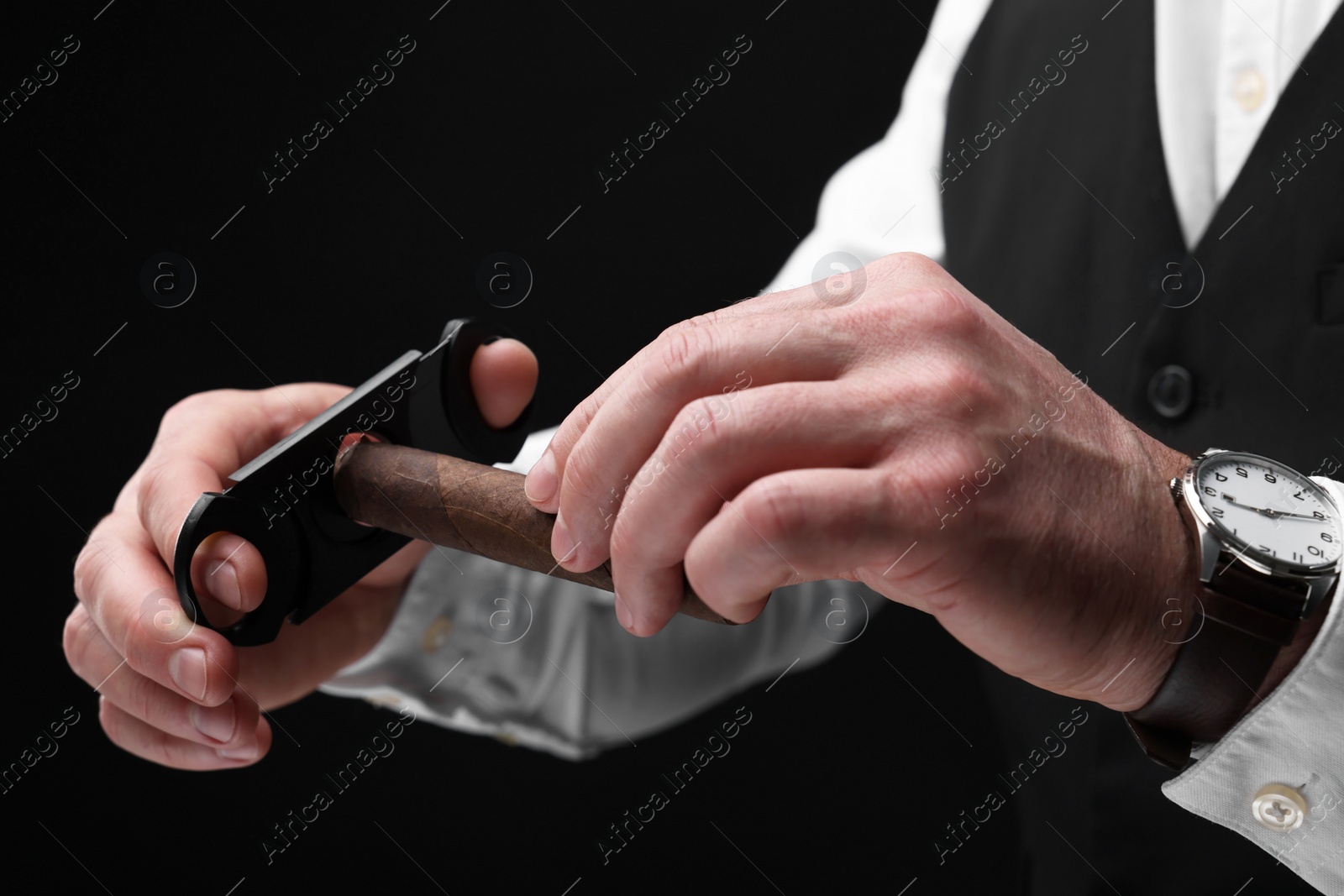 Photo of Man cutting tip of cigar on black background, closeup