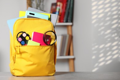 Photo of Yellow backpack with different school stationery on table indoors, space for text