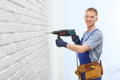 Photo of Handsome young working man using rotary hammer indoors. Home repair