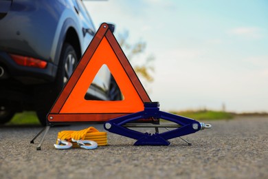 Photo of Emergency warning triangle, towing strap and scissor jack near car outdoors. Safety equipment