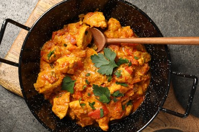 Photo of Delicious chicken curry in frying pan and spoon on grey table, top view