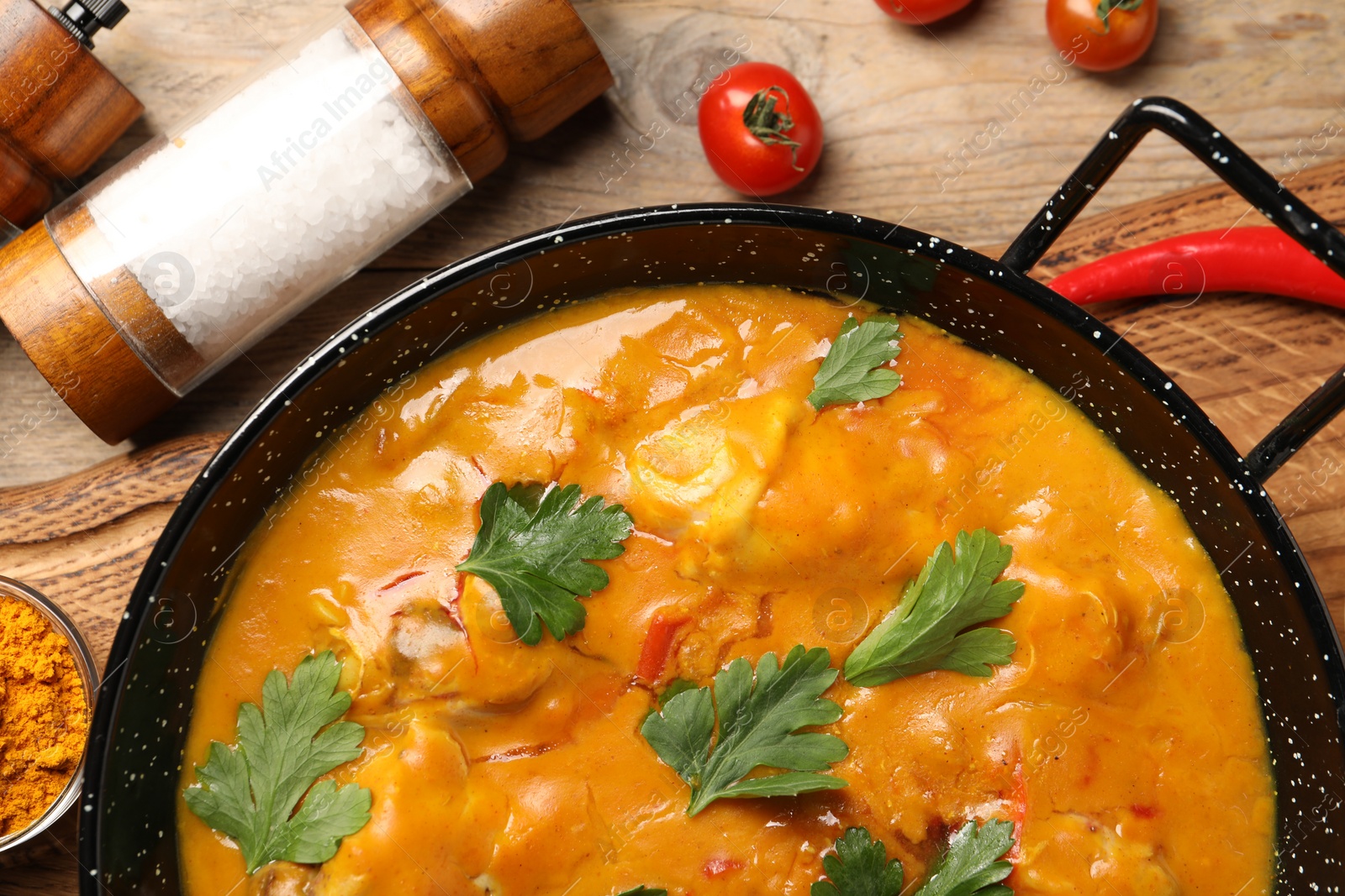 Photo of Tasty chicken curry with parsley and ingredients on wooden table, flat lay