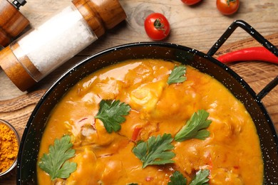 Photo of Tasty chicken curry with parsley and ingredients on wooden table, flat lay