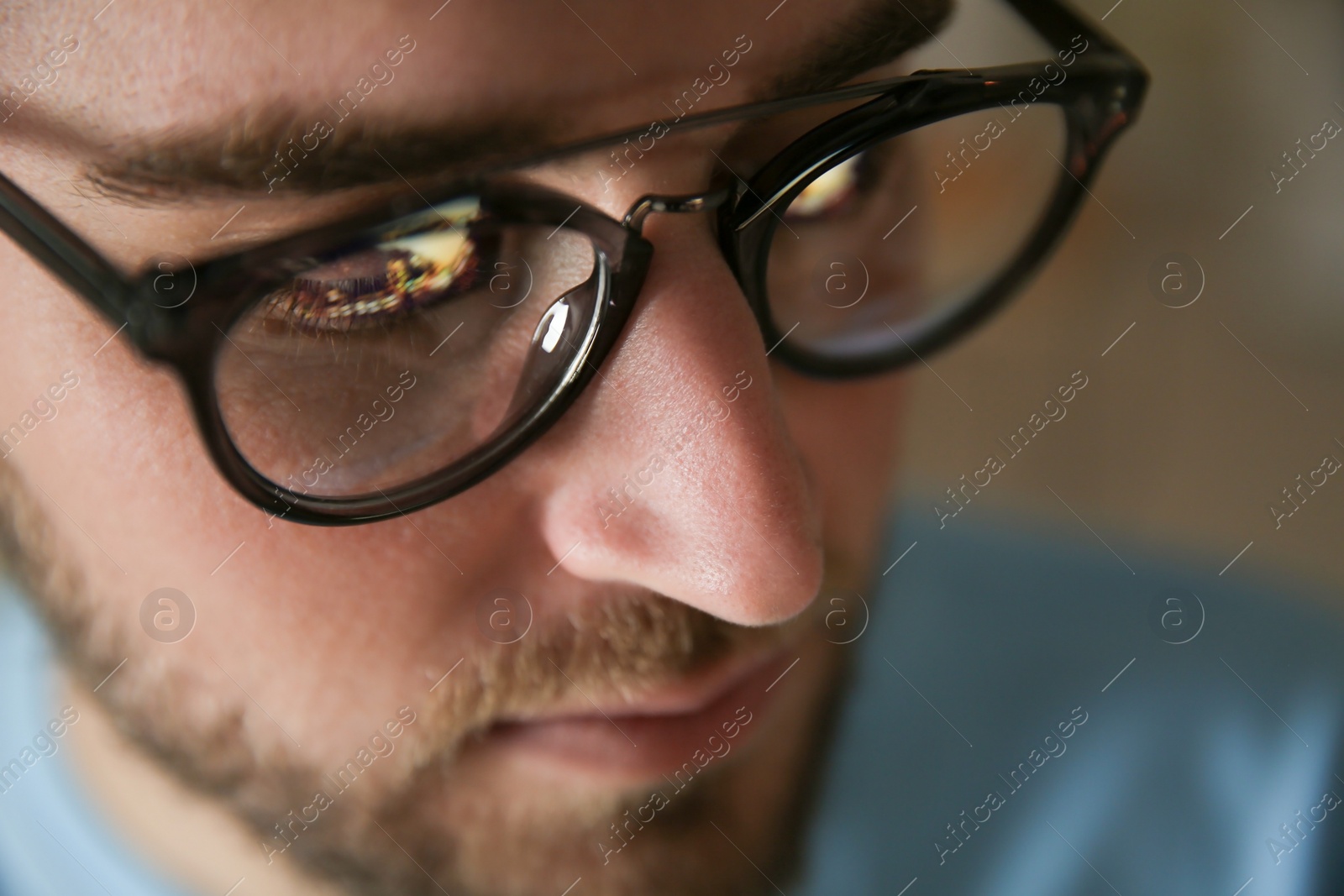 Photo of Young man wearing glasses on blurred background, closeup. Ophthalmology service