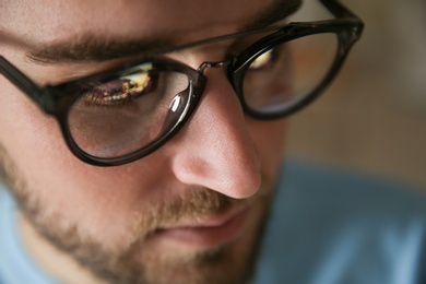 Photo of Young man wearing glasses on blurred background, closeup. Ophthalmology service
