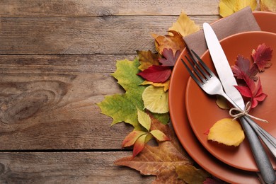 Festive table setting with autumn leaves on wooden background, flat lay. Space for text