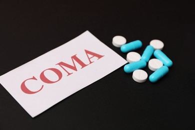 Card with word Coma and pills on black background, closeup