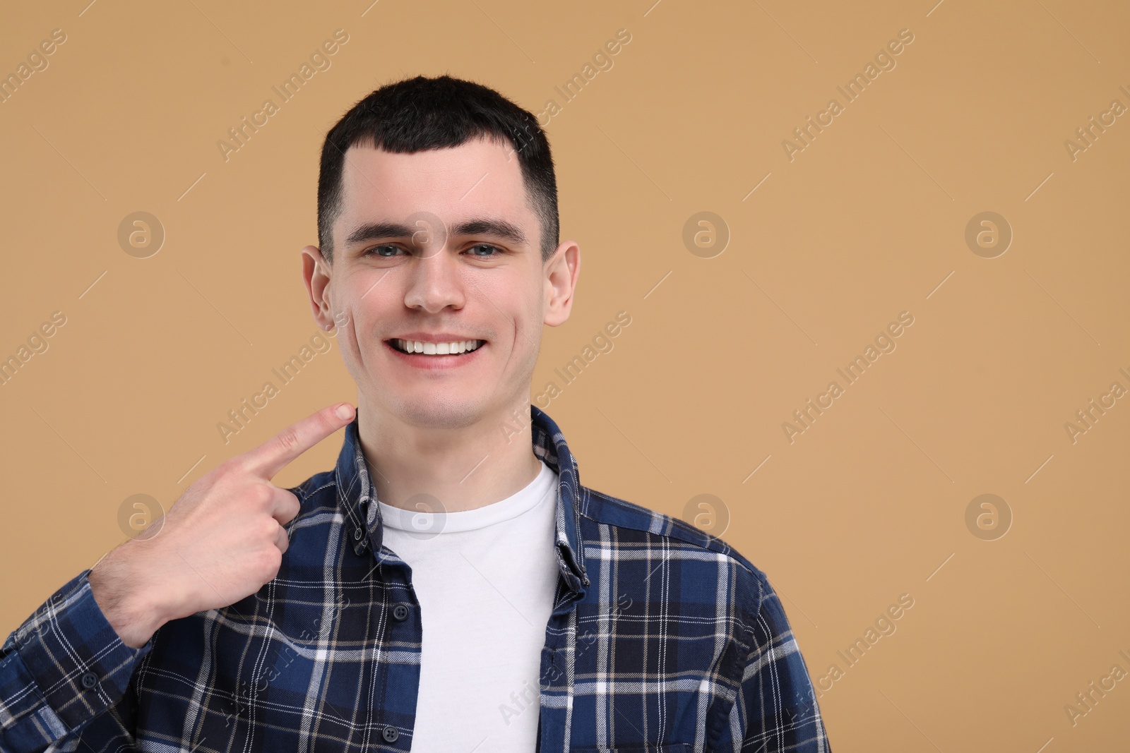 Photo of Handsome young man showing his clean teeth on beige background, space for text