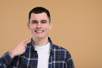 Handsome young man showing his clean teeth on beige background, space for text