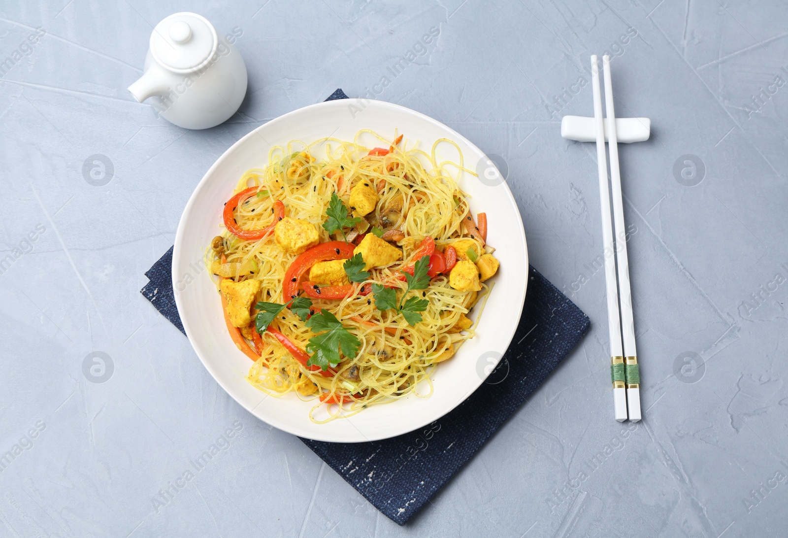 Photo of Stir-fry. Delicious cooked noodles with chicken and vegetables in bowl served on gray textured table, flat lay