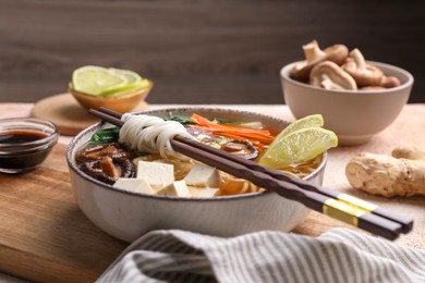 Photo of Bowl of vegetarian ramen and chopsticks on table, closeup
