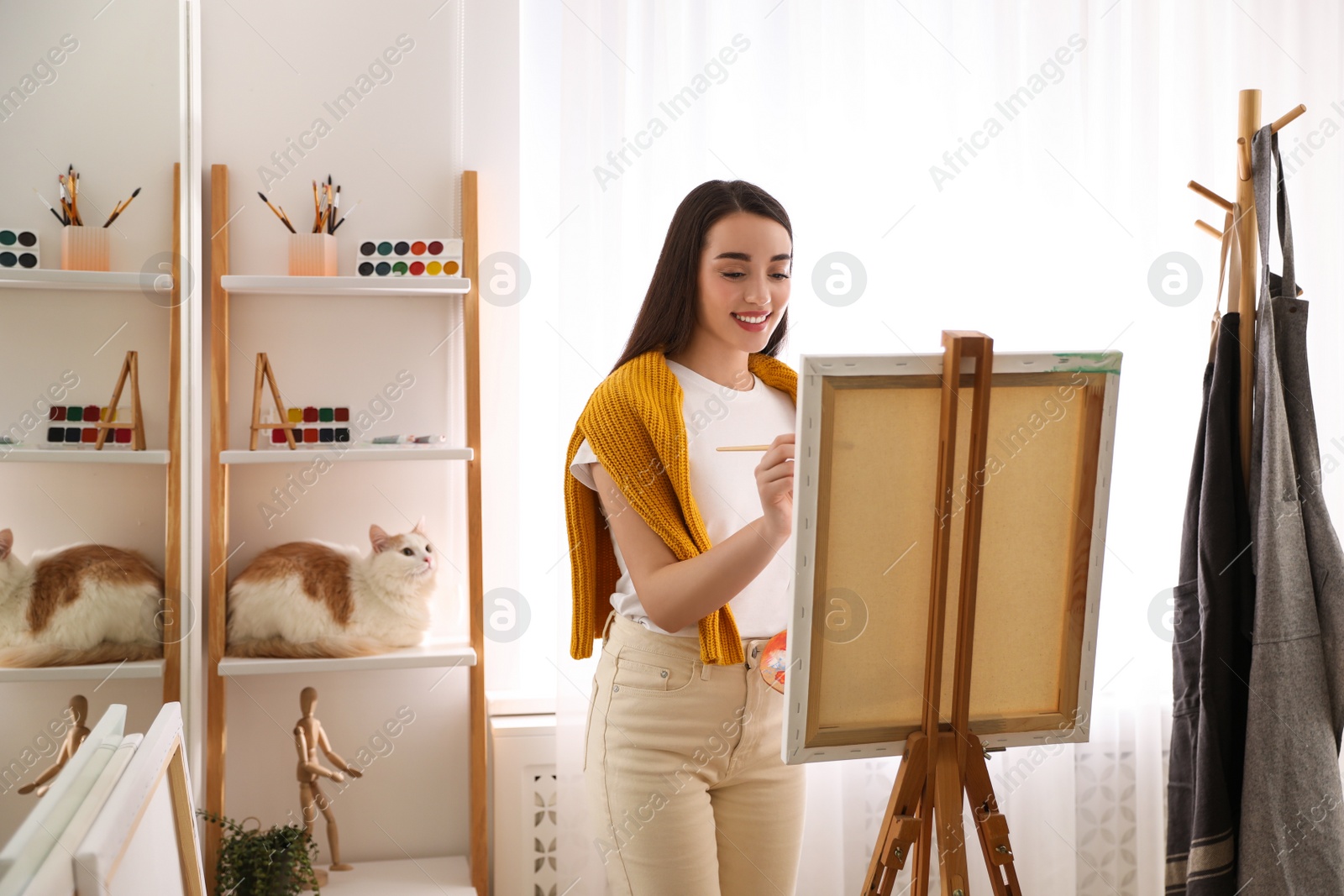 Photo of Beautiful young woman drawing on easel at home