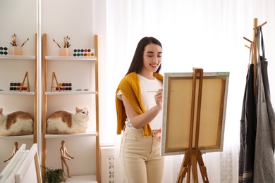 Beautiful young woman drawing on easel at home