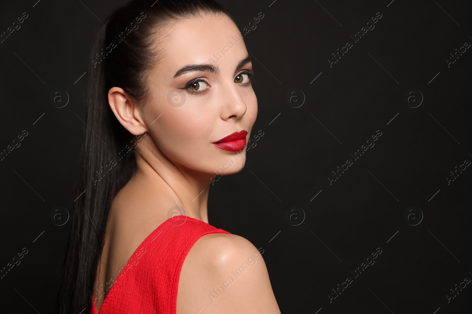 Photo of Portrait of young woman wearing beautiful red lipstick on black background, space for text