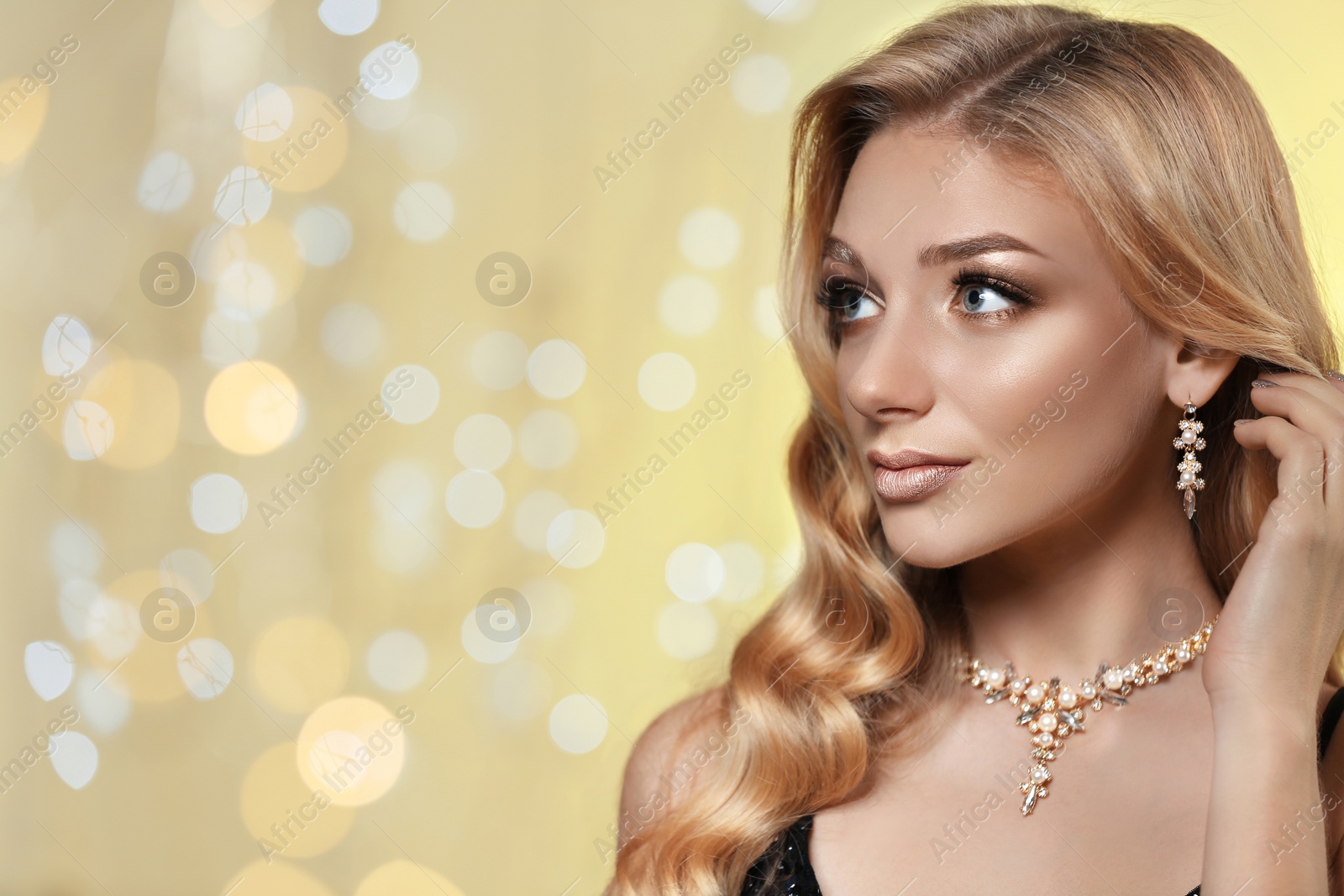 Photo of Beautiful young woman with elegant jewelry against defocused lights. Space for text