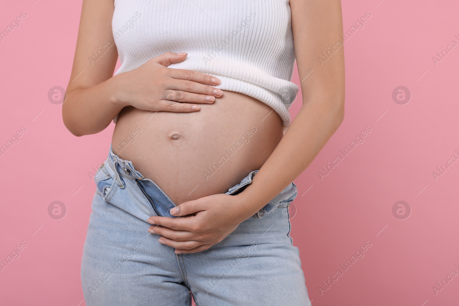 Photo of Pregnant woman in jeans on pink background, closeup