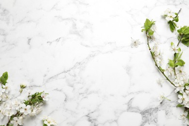 Cherry tree branches with beautiful blossoms on white marble table, flat lay. Space for text