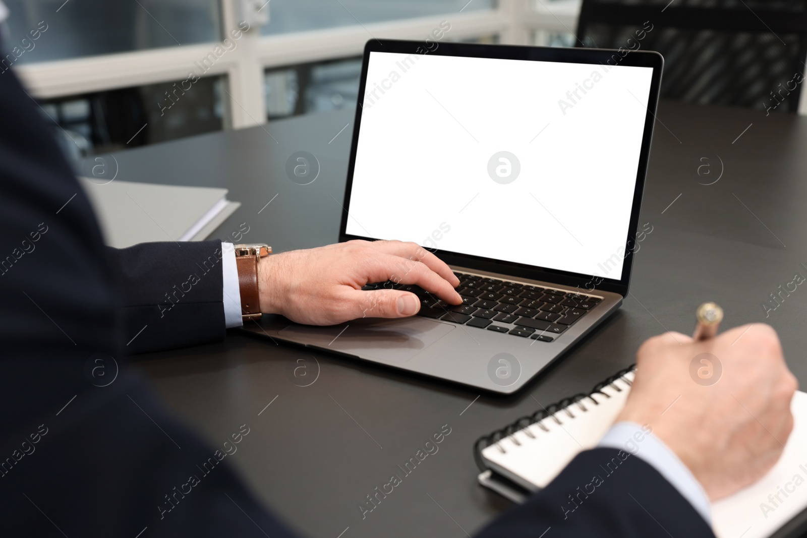 Photo of Man writing notes while working on laptop at black desk in office, closeup