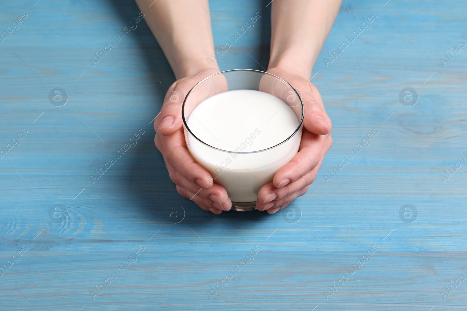 Photo of Woman holding glass of milk at light blue wooden table, closeup