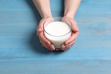 Photo of Woman holding glass of milk at light blue wooden table, closeup