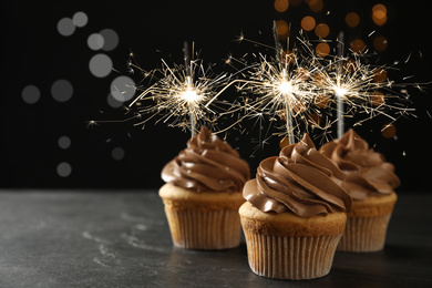 Image of Birthday cupcakes with sparklers on table against dark background. Space for text