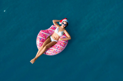 Young woman wearing Santa hat and bikini with inflatable ring in sea, top view. Christmas vacation