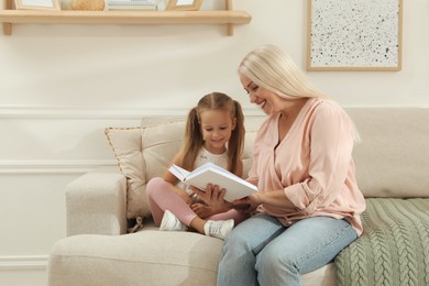 Happy grandmother with her granddaughter reading book together at home