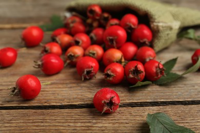 Photo of Ripe rose hip berries with green leaves on wooden table, closeup