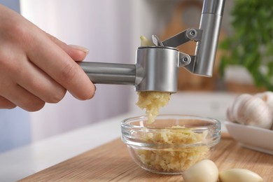 Woman squeezing garlic with press at white table indoors, closeup