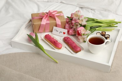 Photo of Tasty breakfast served in bed. Delicious desserts, tea, flowers, gift box and card with phrase I Love You on tray