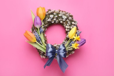 Willow wreath with different beautiful flowers and grey bow on pink background, top view