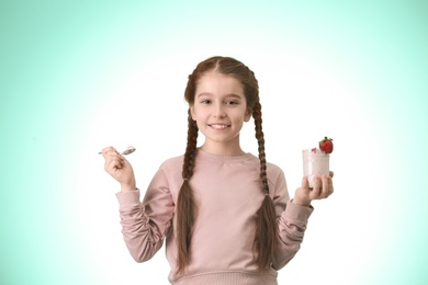 Cute girl eating tasty yogurt on color background