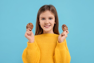 Cute girl with chocolate chip cookies on light blue background