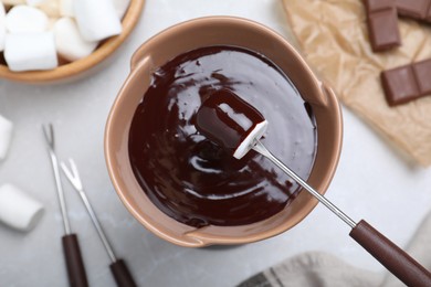 Photo of Dipping marshmallow into melted chocolate on light grey marble table, flat lay