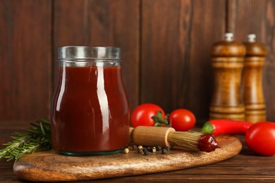 Photo of Tasty barbecue sauce in glass jar, brush and ingredients on wooden table, closeup