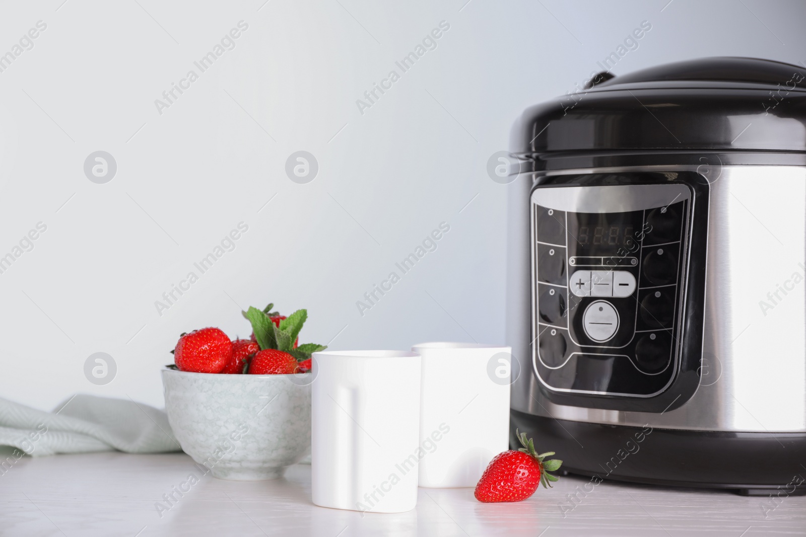 Photo of Cups of homemade yogurt, strawberries and multi cooker on table