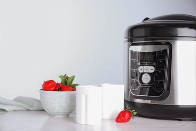 Cups of homemade yogurt, strawberries and multi cooker on table