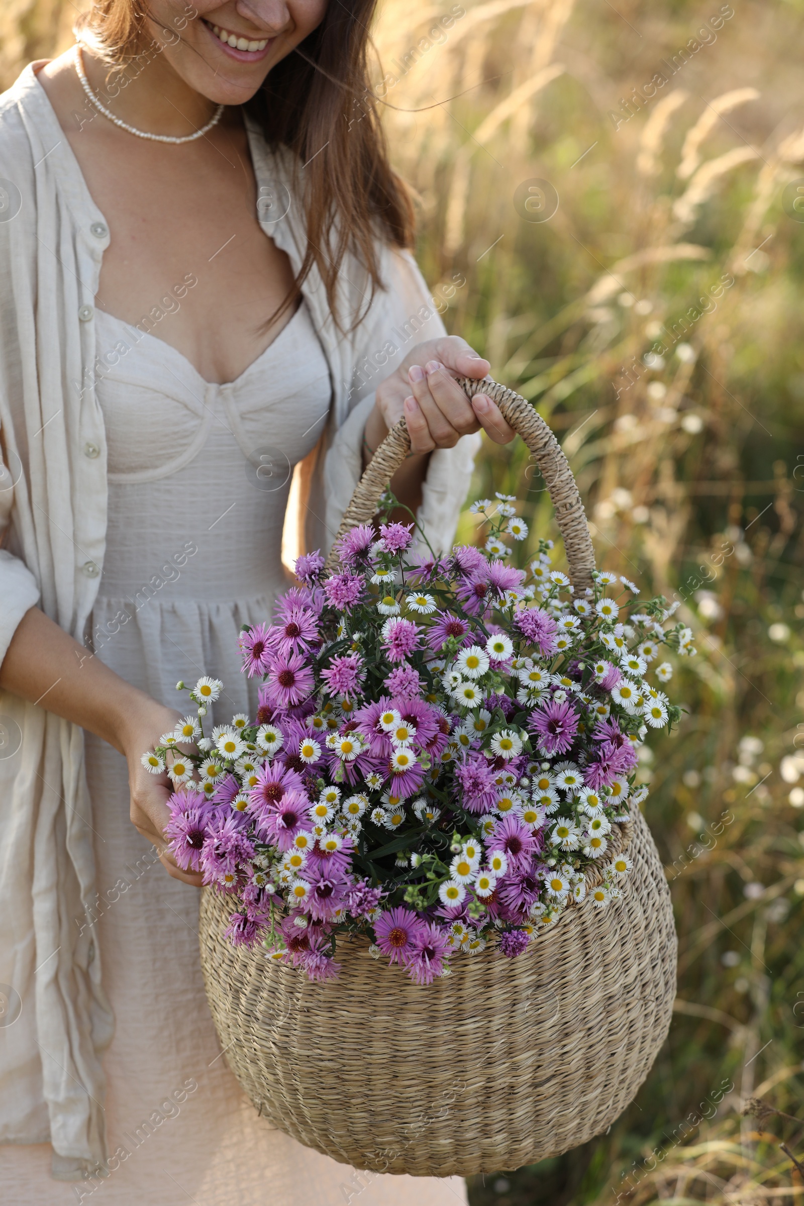 Photo of Woman holding wicker basket with beautiful wild flowers outdoors, closeup