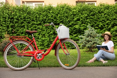 Photo of Young woman sitting near modern bicycle on grass outside