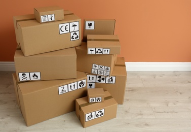 Photo of Cardboard boxes with different packaging symbols on floor near orange wall. Parcel delivery