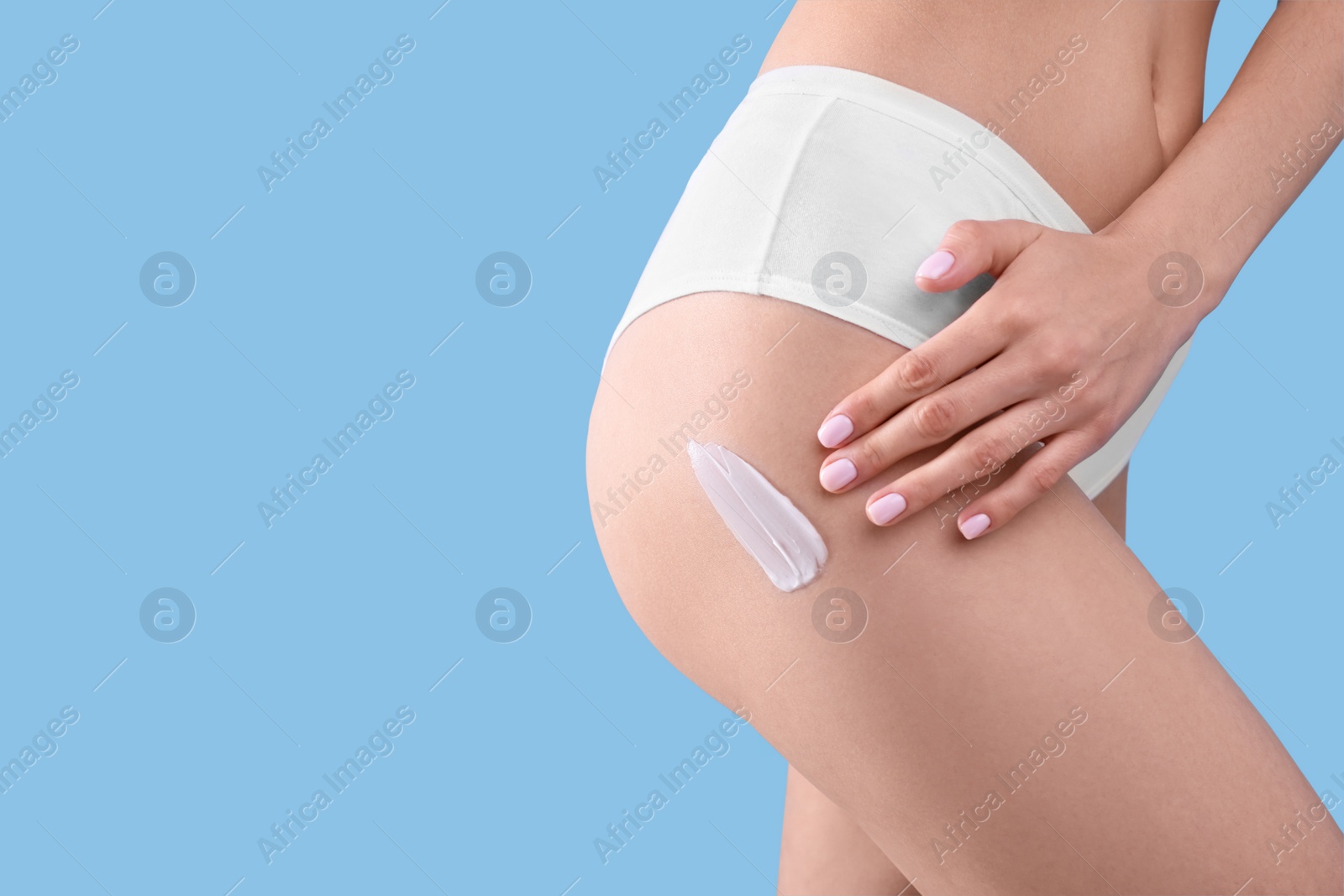 Photo of Woman with smear of body cream on her leg against light blue background, closeup. Space for text