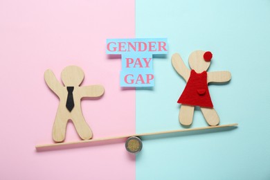 Photo of Gender pay gap. Wooden figures of man and woman on miniature seesaw against color background, flat lay