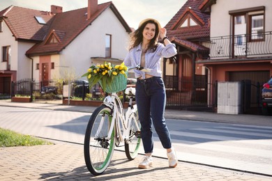 Photo of Beautiful woman with bicycle and bouquet of yellow tulips on city street