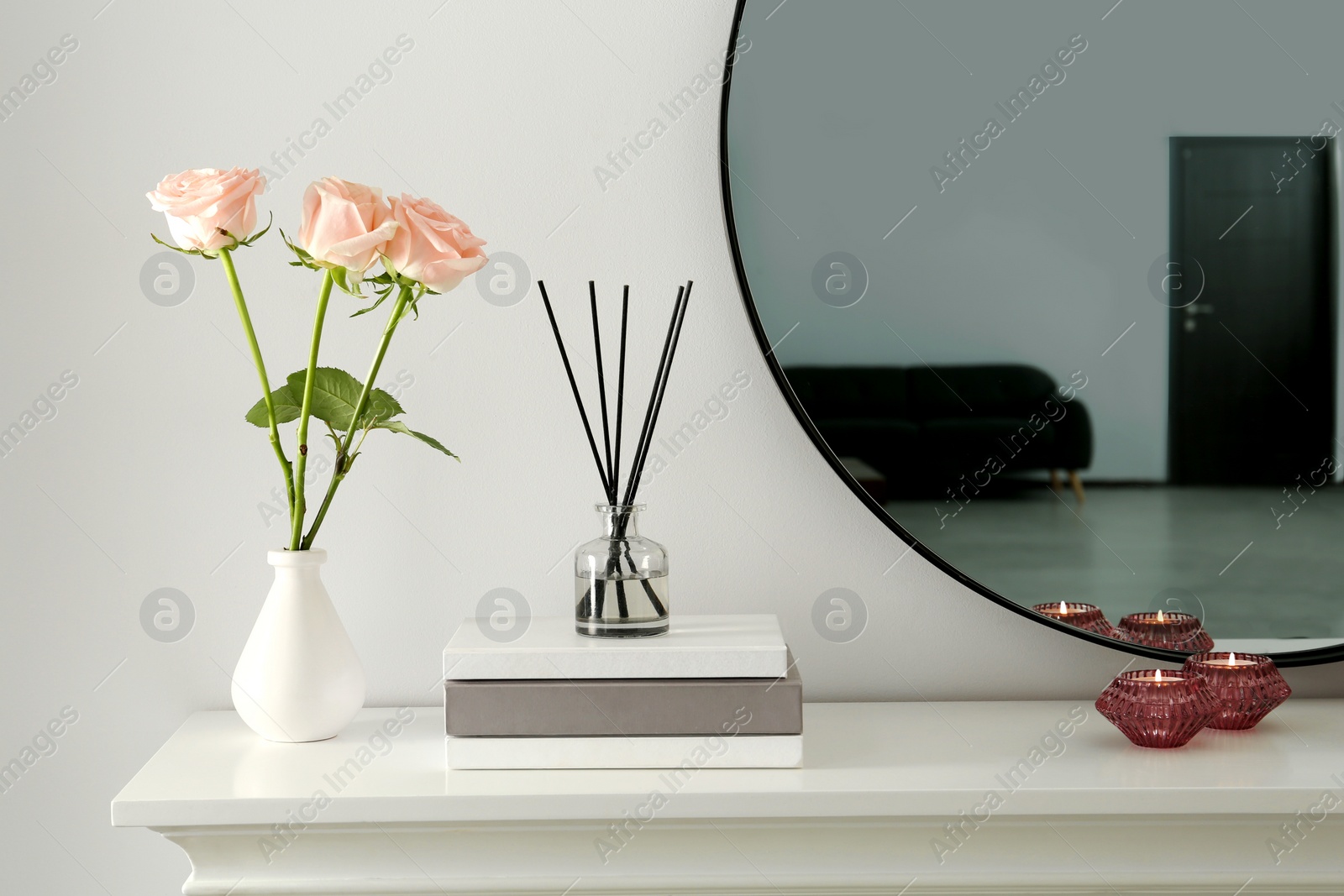 Photo of Roses, candles and reed diffuser on white console table in room