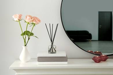 Roses, candles and reed diffuser on white console table in room